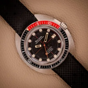 A vintage Bulova Oceanographer Automatic Snorkel 714 Red Cross Hair Dial watch featuring a black dial, red and black bezel, and a textured black strap.