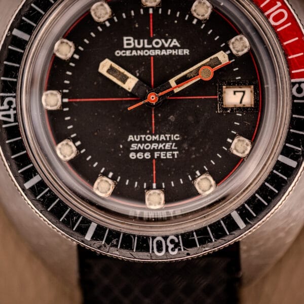 Close-up of the Bulova Oceanographer Automatic Snorkel 714 Red Cross Hair Dial watch, featuring a date display set to 7 and water resistance rated at 666 feet.