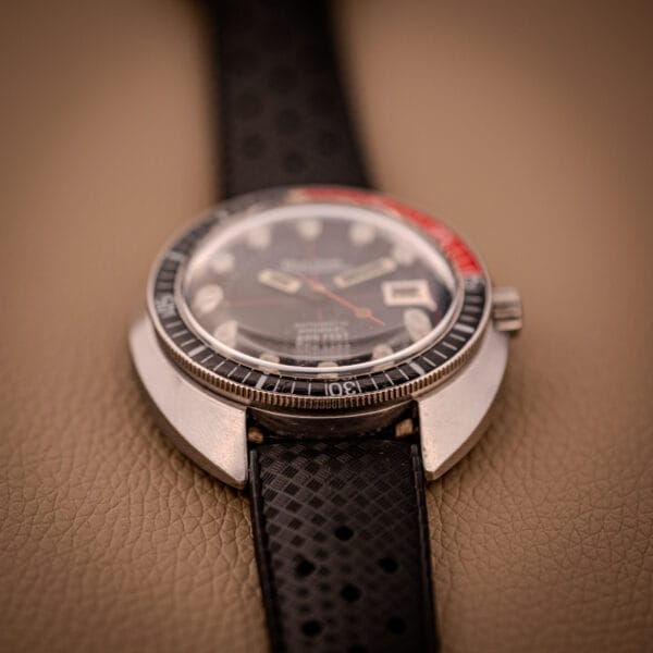 A close-up of the Bulova Oceanographer Automatic Snorkel 714 with a Red Cross Hair Dial, displayed on a textured beige surface.