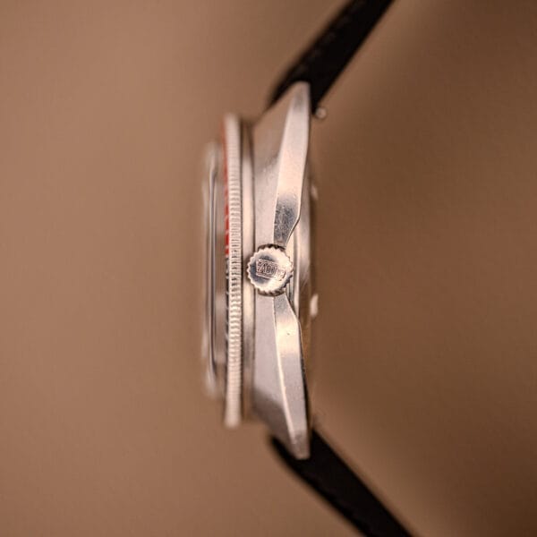 Side view of a Bulova Oceanographer Automatic Snorkel 714 Red Cross Hair Dial wristwatch with a black strap, set against a brown background.