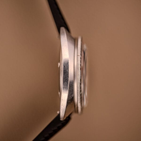 Side view of the Bulova Oceanographer Automatic Snorkel 714 with Red Cross Hair Dial, metal case, and black strap, set against a beige background.