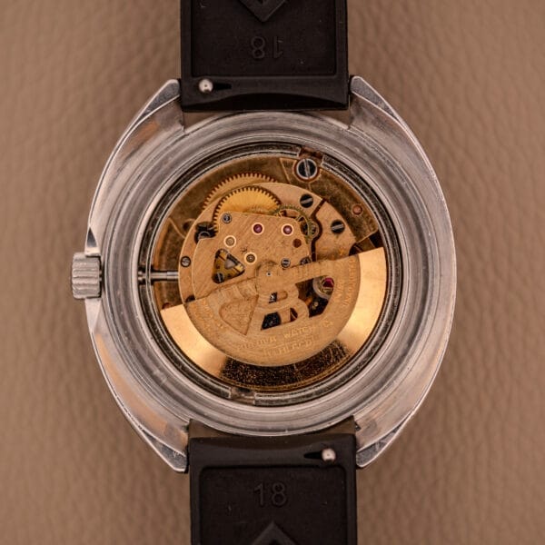 Close-up of the Bulova Oceanographer Automatic Snorkel 714 Red Cross Hair Dial’s transparent case back, showcasing its intricate gold mechanical movement and remarkable craftsmanship.