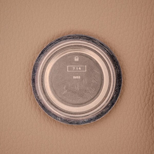 A round metal watch case back marked 714 SWISS, likely from a Bulova Oceanographer Automatic Snorkel 714 Red Cross Hair Dial, rests on a textured beige surface.