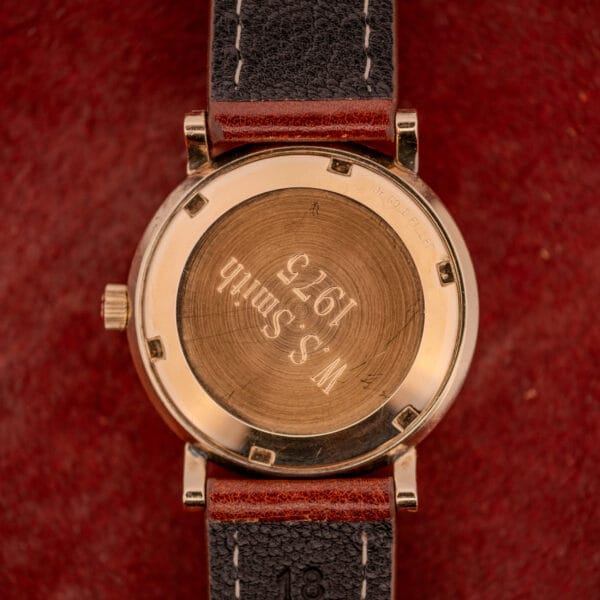 An Omega Automatic Seamaster Date Ref. KM 6323 Cal. 563 with “W.S. Smith 1975” engraved on the back rests on a red textured surface.