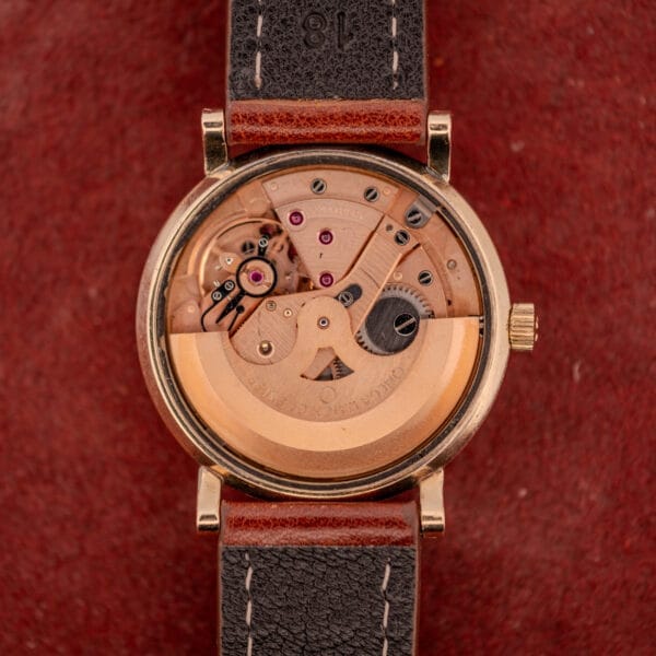 Omega Automatic Seamaster Date Ref. KM 6323 Cal. 563 mechanical watch with visible gears and movement, brown leather strap, displayed on red fabric.
