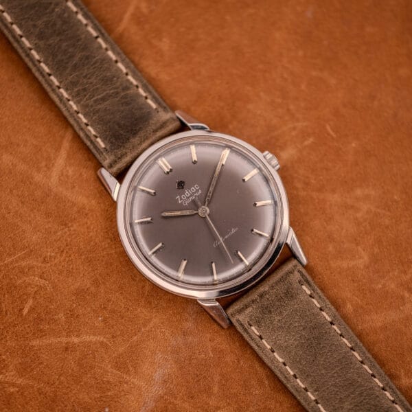 A Zodiac Glorious Automatic Ref. 702-917 wristwatch with a brown leather strap rests on a brown leather surface, its stainless steel case highlighting the elegance of the Cal. 70-72 movement.