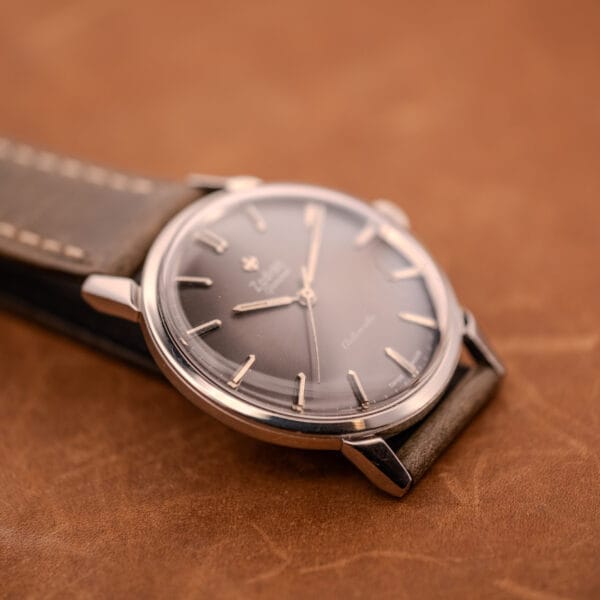 A Zodiac Glorious Automatic Ref. 702-917 wristwatch with stainless steel case and brown leather strap sits on a matching surface, showcasing the refined style of Cal. 70-72 craftsmanship.