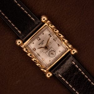 Gruen 21 Precision Art Deco Twisted Rope Case Ref. 335/530 wristwatch with a white dial and black leather strap, displayed on a brown background.