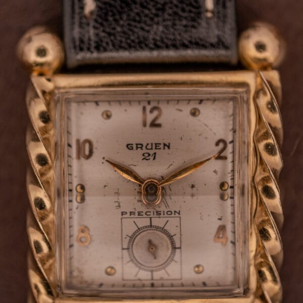 Close-up of a Gruen 21 Precision Art Deco Twisted Rope Case Ref. 335/530 wristwatch featuring a gold frame and black leather strap.