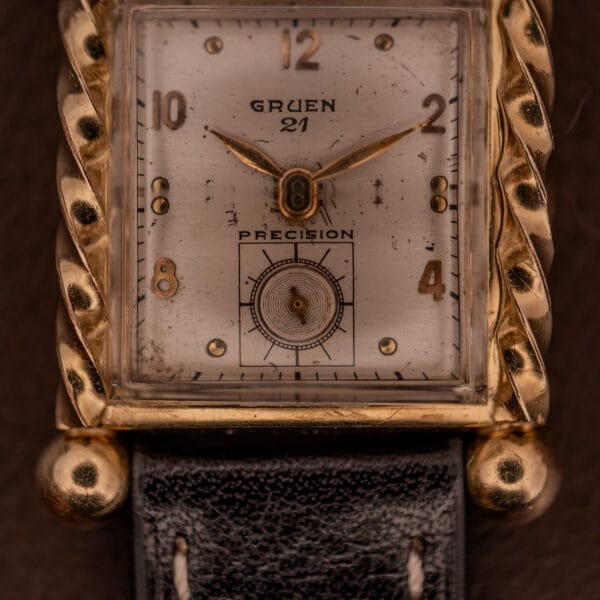 Close-up of a Gruen 21 Precision Art Deco Twisted Rope Case Ref. 335 / 530 gold wristwatch with a black leather strap.