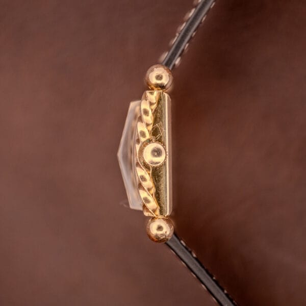 Close-up of a gold decorative clasp with round details on brown leather, evoking Art Deco style and the refined elegance of the Gruen 21 Precision Art Deco Twisted Rope Case Ref. 335 / 530.