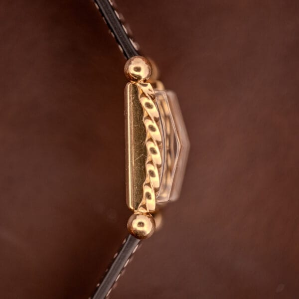 Close-up of the gold decorative clasp with a twisted rope design on the Gruen 21 Precision Art Deco Twisted Rope Case Ref. 335 / 530, shown on a brown leather surface.