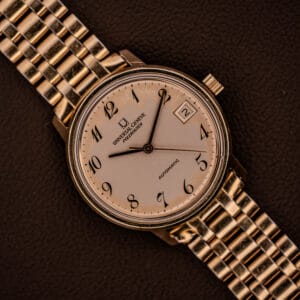 Universal Geneve Polerouter Date with white Arabic numerals dial, automatic Cal 215 movement, and classic style. Displayed on a textured brown surface.