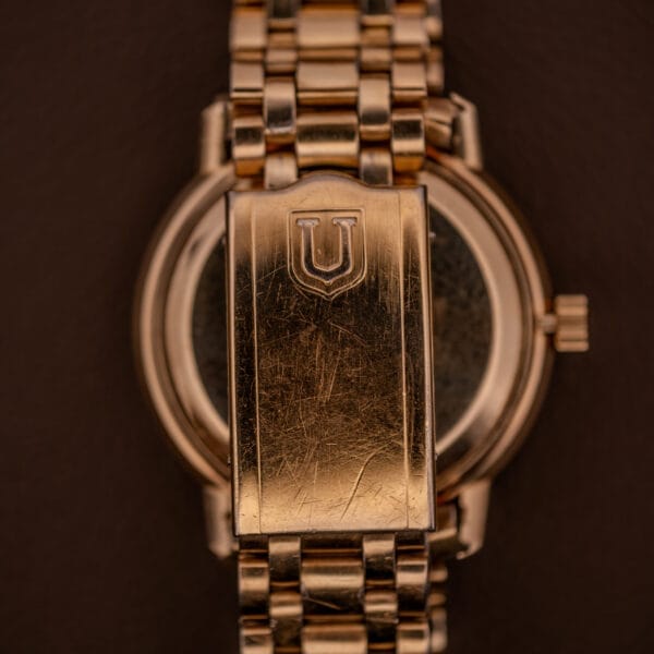 Universal Geneve Polerouter Date with Arabic numerals dial, Automatic Cal 215 movement, gold case and metal link band, clasp engraved with "U," displayed against a dark background.