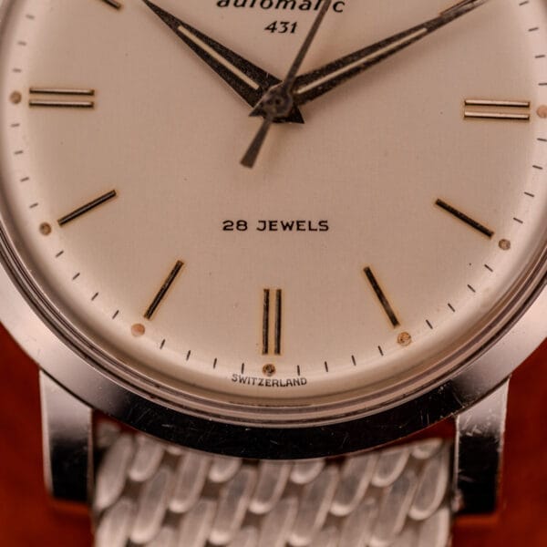 Close-up of a Movado Automatic 431 Ref. 11201 wristwatch face featuring "28 JEWELS" and "SWITZERLAND" above its stainless steel case and bracelet.