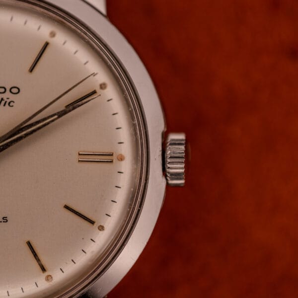 Close-up of the Movado Automatic 431 Ref. 11201 with a stainless steel case and bracelet, highlighting the crown and part of the dial against a brown background.