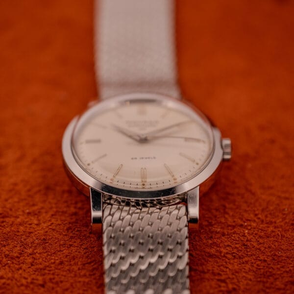 A Movado Automatic 431 Ref. 11201 with a stainless steel case and bracelet is displayed on an orange textured surface.
