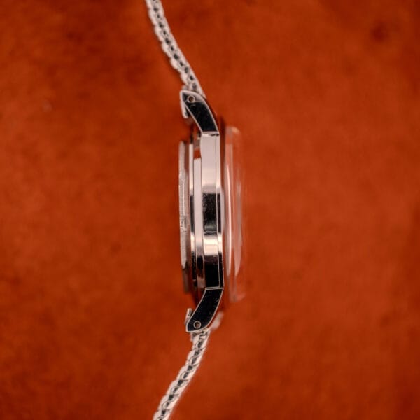 Side view of a Movado Automatic 431 Ref. 11201 wristwatch with a stainless steel case and bracelet on a textured orange background.