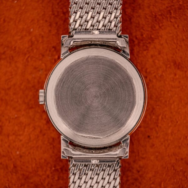 A Movado Automatic 431 Ref. 11201 with a stainless steel case and bracelet is shown from the back as it rests on a textured orange surface.