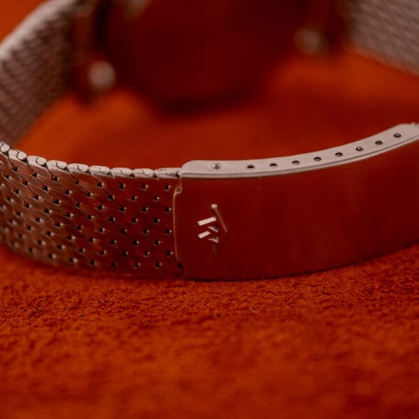 Close-up of the Movado Automatic 431 Ref. 11201 stainless steel clasp with logo, on an orange textured surface.