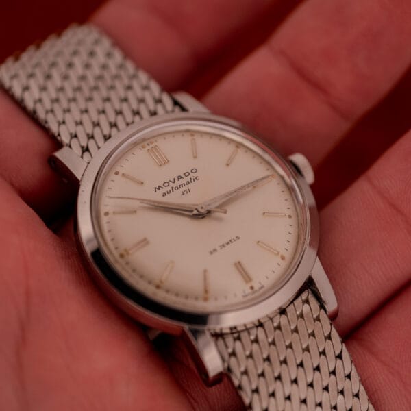 A Movado Automatic 431 wristwatch, Ref. 11201, with a stainless steel case and bracelet, held in someone's hand.