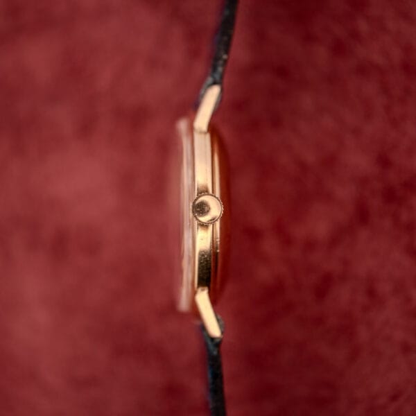 Side view of a slim Girard Perregaux Gyromatic White Dial & Gold Arabic Numerals wristwatch with a black strap, shown against a textured red background.