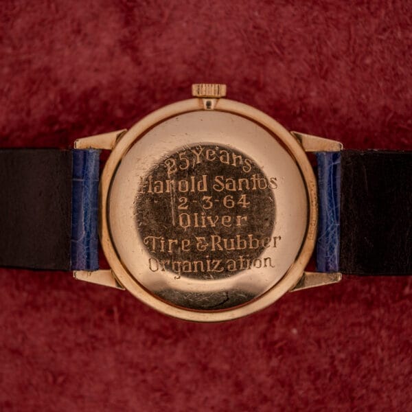Girard Perregaux Gyromatic White Dial & Gold Arabic Numerals watch, with back engraved "25 Years Harold Santos 2-3-64 Oliver Tire & Rubber Organization," displayed on red fabric.