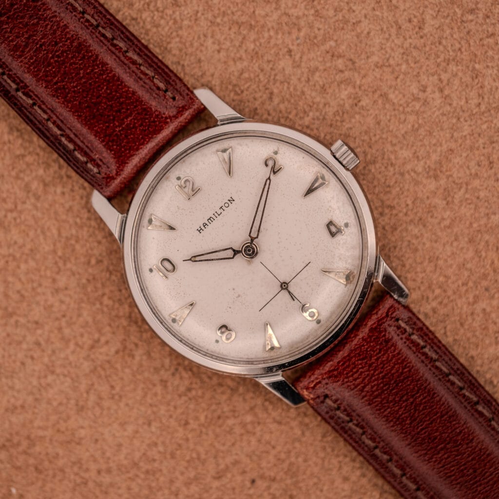 The Hamilton Sea-Crest Stainless Steel Case & White Dial Cal. 673 wristwatch with a brown leather strap rests on a tan textured surface.