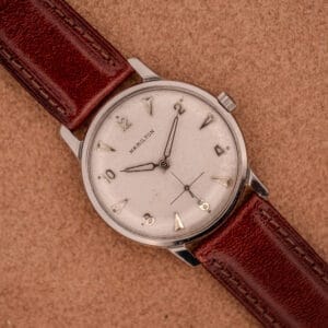 The Hamilton Sea-Crest Stainless Steel Case & White Dial Cal. 673 wristwatch with a brown leather strap rests on a tan textured surface.