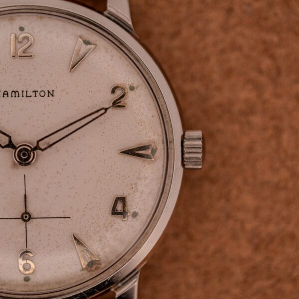 Close-up of a Hamilton Sea-Crest Stainless Steel Case & White Dial Cal. 673 wristwatch showing 10:10, set against a brown textured background.