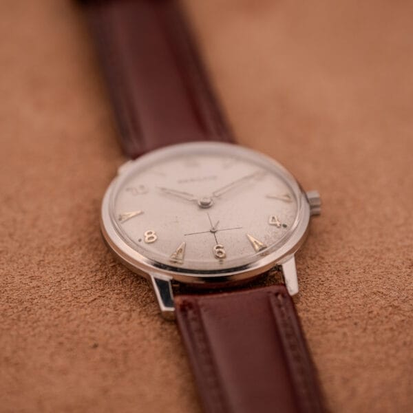 A Hamilton Sea-Crest Stainless Steel Case & White Dial Cal. 673 wristwatch with a brown leather strap, displayed on a tan textured surface.