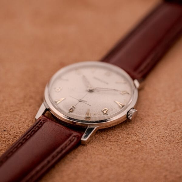 The Hamilton Sea-Crest Stainless Steel Case & White Dial Cal. 673 wristwatch with a brown leather strap rests elegantly on a soft tan surface, showcasing classic style and timeless appeal.