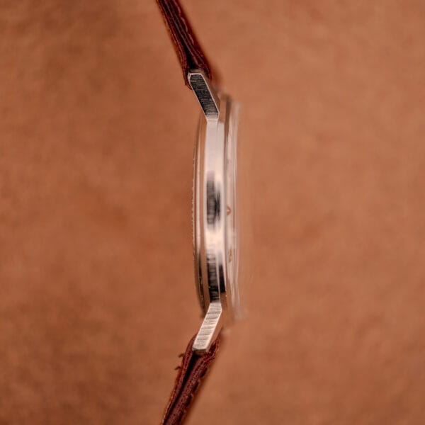 Close-up side view of the Hamilton Sea-Crest Stainless Steel Case & White Dial Cal. 673 wristwatch with a brown leather strap, set against a brown background.