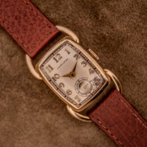 A Hamilton Bowman Art Deco 10k Gold Filled Case Manual Wind Cal. 980 wristwatch with a brown leather strap rests on a textured surface, highlighting its vintage charm and classic style.