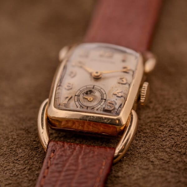 Close-up of a Hamilton Bowman Art Deco wristwatch with a 10k Gold Filled case and manual wind Cal. 980 movement, showcasing its vintage dial and brown leather strap on a textured surface.