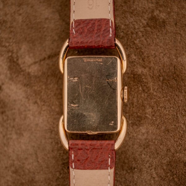 A scratched Hamilton Bowman Art Deco 10k Gold Filled Case Manual Wind Cal. 980 wristwatch with a brown leather strap, displayed from the back on a brown surface.