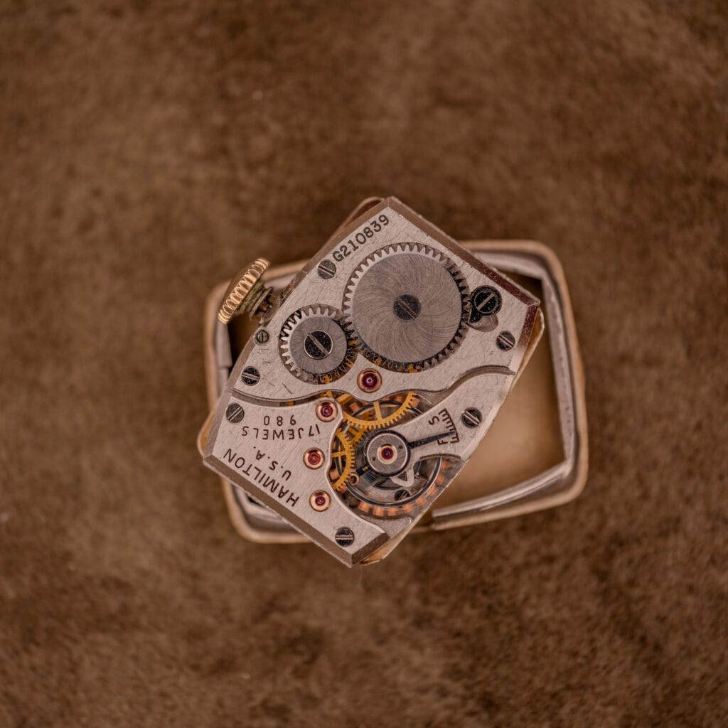 A close-up of an open Hamilton Bowman Art Deco 10k Gold Filled Case Manual Wind Cal. 980 watch, showcasing its intricate mechanism against a brown textured surface.