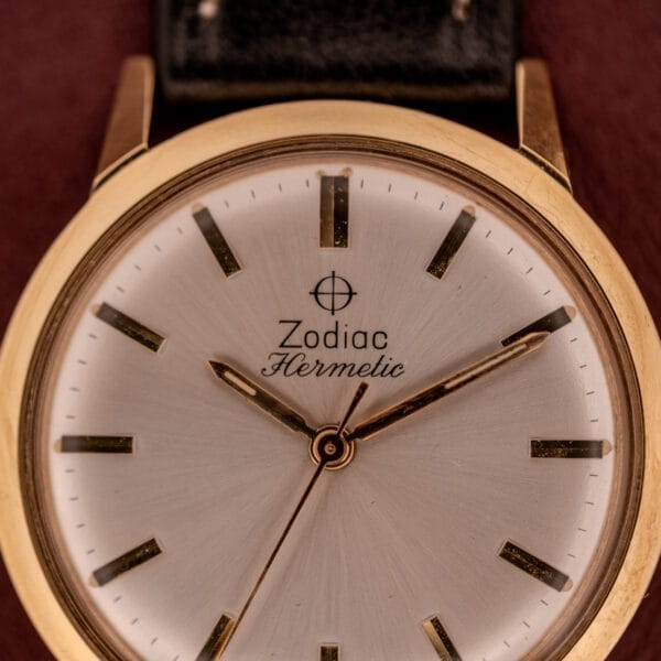 Close-up of a Zodiac Hermetic Ref. 673 853 wristwatch with a sunburst dial, displaying 9:11:32, set against a brown background. Includes original box and papers.