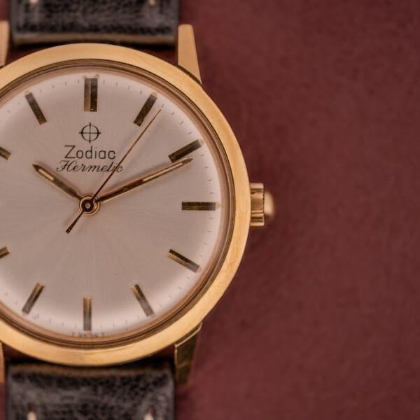 Close-up of the Zodiac Hermetic Ref. 673 853 Sunburst Dial wristwatch with a leather strap, displayed on a textured burgundy background. Includes original box and papers.