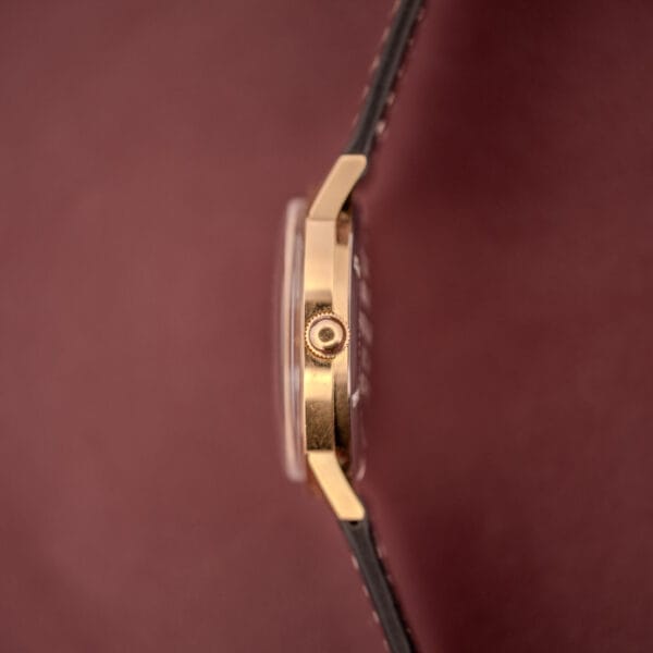 Side view of the Zodiac Hermetic Ref. 673 853 with a gold sunburst dial and black leather band, shown against a maroon background. Includes original box and papers.