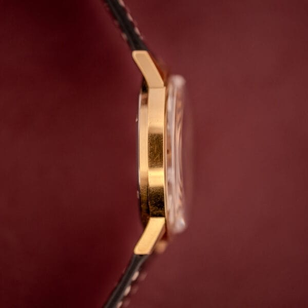 Side view of the Zodiac Hermetic Ref. 673 853 Sunburst Dial wristwatch with a black leather strap, shown against a burgundy background; includes original box and papers.