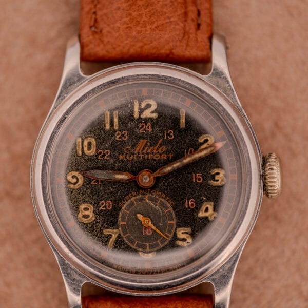 A vintage Mido Multifort Super-Automatic Bumper wristwatch featuring a black and red military dial and brown leather strap.