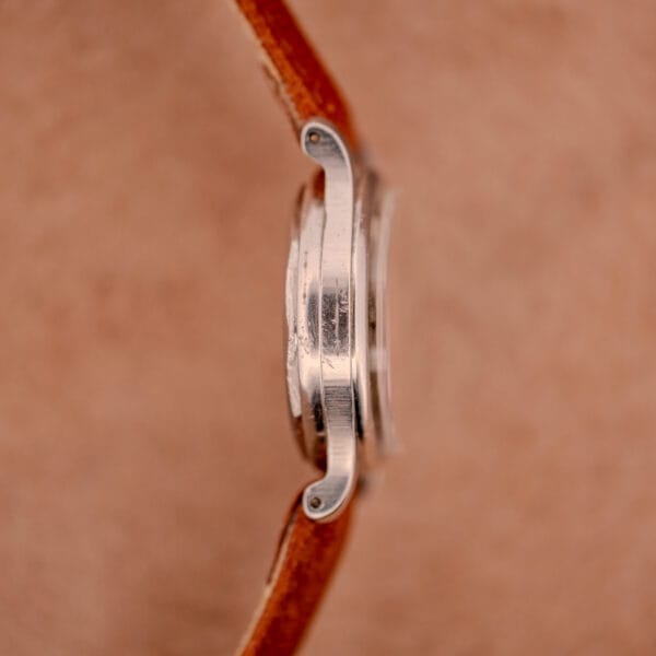 Side view of the Mido Multifort Super-Automatic Bumper with brown leather straps and a black & red military dial on a soft beige background.