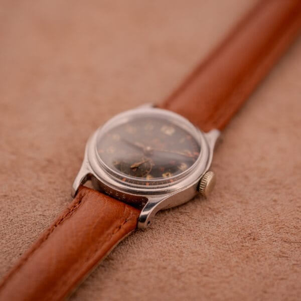 A vintage Mido Multifort Super-Automatic Bumper wristwatch with a black & red military dial rests elegantly on a soft beige surface.