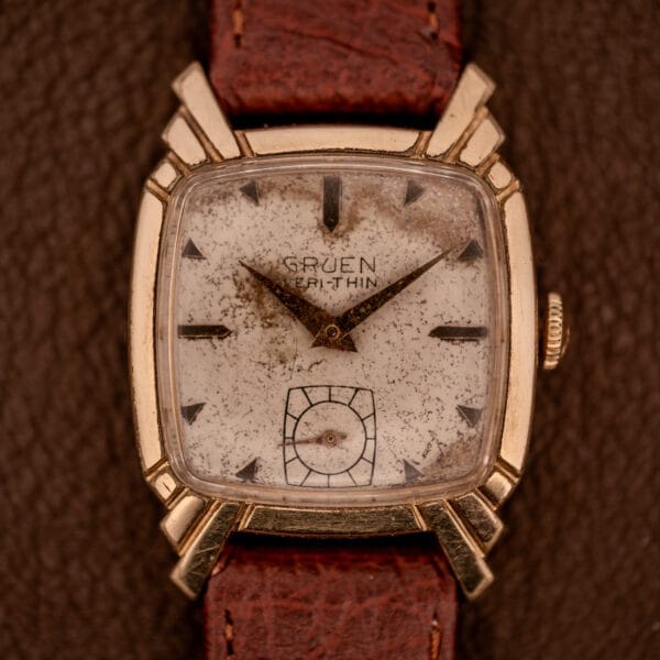 A Gruen Veri-Thin Ref. 415-810 wristwatch with Art Deco lugs and a brown leather strap rests elegantly on a brown surface.