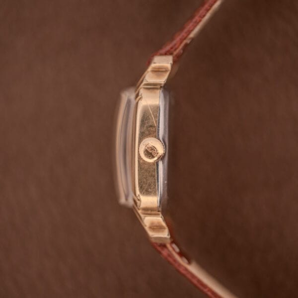 Side view of a Gruen Veri-Thin Ref. 415-810 wristwatch with Art Deco lugs, manual wind Cal. 415 movement, and a brown leather strap on a brown background.