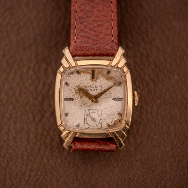 A Gruen Veri-Thin Ref. 415-810 wristwatch with classic Art Deco lugs and manual wind Cal. 415 rests on a brown textured surface, exuding vintage charm with its brown leather strap.