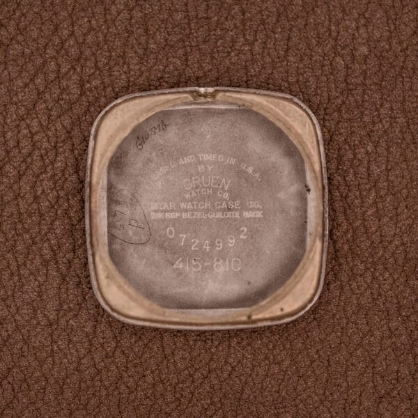 Square metal case back engraved with Gruen Veri-Thin Ref. 415-810 branding and serial numbers, set against a textured brown background, complemented by distinctive Art Deco lugs and manual wind Cal. 415 movement.