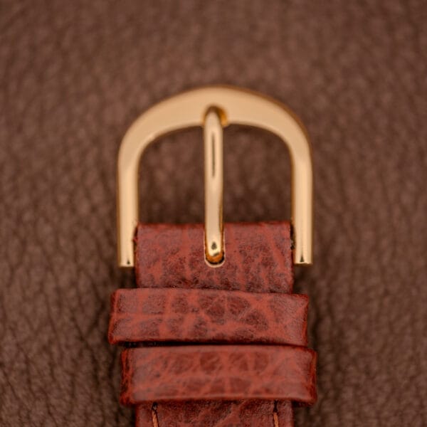 Close-up of the gold buckle on the Gruen Veri-Thin Ref. 415-810’s brown leather strap with Art Deco lugs, set against a textured brown background.