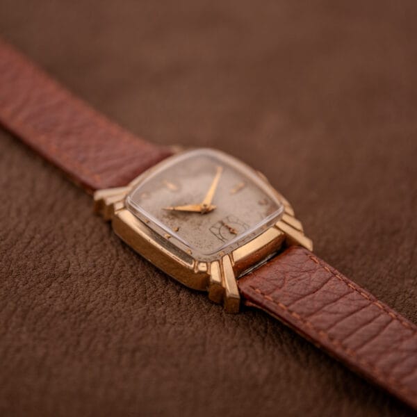 A Gruen Veri-Thin Ref. 415-810 with Art Deco lugs and a brown leather strap rests on a brown textured surface. This manual wind watch features the Cal. 415 movement, capturing classic vintage style.
